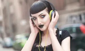 Mroczna goth girl w słuchawkach, z czarną szminką i kolczykiem w nosie, słucha muzyki na ulicy.