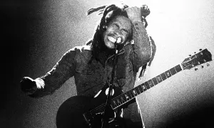 Bob Marley z gitarą, w transie, śpiewa na scenie. Jego dredy unoszą się w powietrzu, a ręka sięga do głowy. To ikona muzyki, której rytmy ska porwały tłumy.