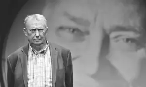 Wojciech Młynarski, jakby z tekstu "Jesteśmy na wczasach", w okryciu w kratę, na tle swojego portretu.