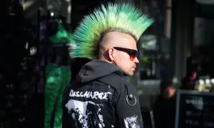 Mężczyzna z zielonym irokezem, w okularach przeciwsłonecznych i kurtce z naszywkami. Jego styl to czysty punk.