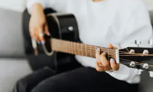 Dłoń z niebieskim lakierem na paznokciach gra na czarnej gitarze, tworząc rytmy w stylu reggae.