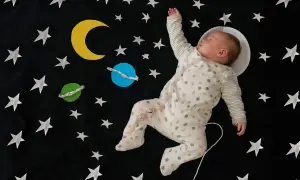 Śpiące dziecko w piżamce w kropki, otoczone gwiazdami i planetami, jakby leciało w kosmos. Ach śpij kochanie tekst pasuje do tej sceny.