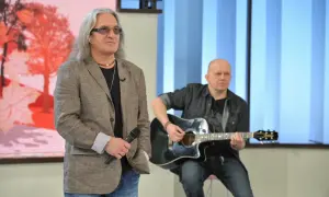 Mężczyzna z mikrofonem i długimi włosami, obok niego siedzi drugi mężczyzna grający na gitarze. Może to być idealny tekst kołysanki dla nieznajomej.