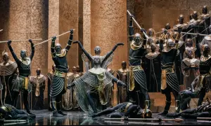 Scena z opery Aida: tancerze w czarnych strojach ze złotymi zdobieniami i maskami na twarzach, niektórzy z włóczniami, inni leżą na scenie.