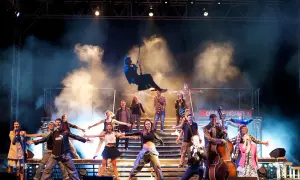 Scena z musicalu "Musical Metro" z aktorami w dynamicznych pozach, dymem i światłami.