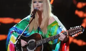 Maryla Rodowicz, ile ma lat, w kolorowym stroju gra na gitarze dwunastostrunowej na scenie.
