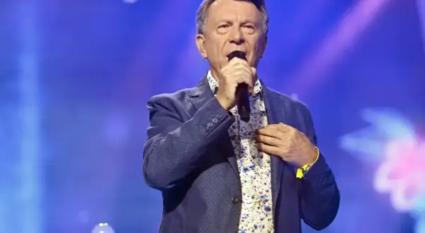 Wojciech Gąsowski w niebieskiej marynarce i kwiecistej koszuli śpiewa do mikrofonu na tle niebieskiej sceny.