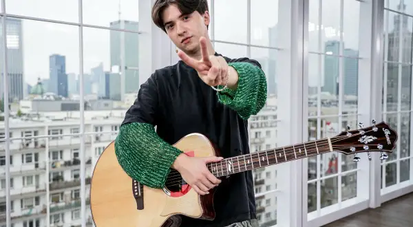 Młody muzyk z gitarą, pozdrawia gestem pokoju. Może właśnie tworzy nowe, popularne piosenki.
