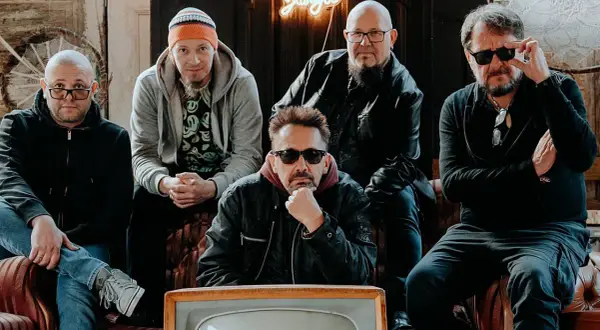 Pięciu mężczyzn, zespół Sztywny Pal Azji, siedzi na kanapie. W tle neonowy napis "Jungle".