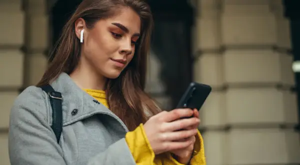 Kobieta w słuchawkach bezprzewodowych korzysta z telefonu.