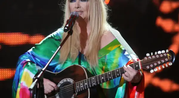 Maryla Rodowicz, ile ma lat, w kolorowym stroju gra na gitarze dwunastostrunowej na scenie.