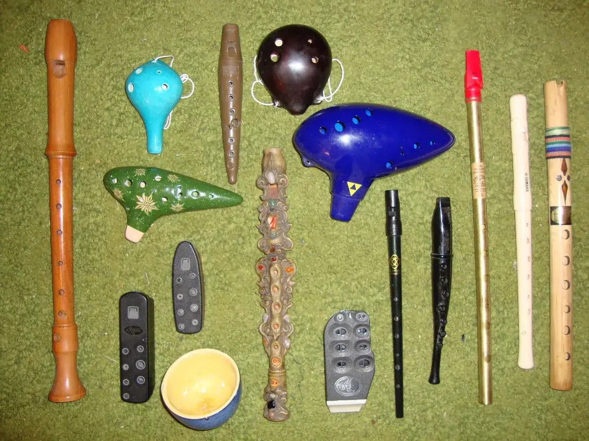 Kolekcja instrumentów dętych: drewniana flauta, niebieska i zielona ocarina, ciemnobrązowa ocarina, niebieska ocarina w kształcie stworka, ozdobna fletnia Pana, kilka mniejszych fletów i bambusowy flet.